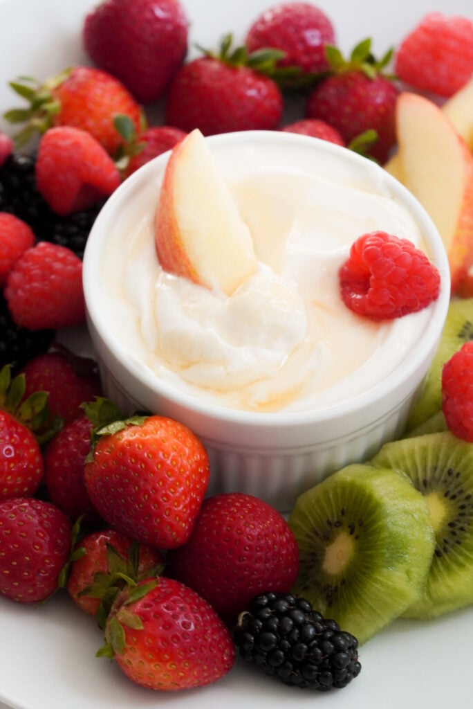 healthy fruit yogurt dip platter with fresh whole strawberries, raspberries, and blackberries plus slices of light red apples and kiwis.