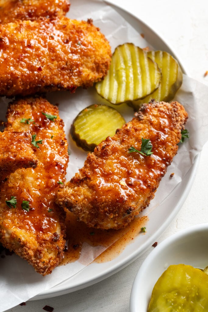 half of a white dinner plate with crispy air fried honey hot chicken tenders; the breading is crispy and golden and almost looks truly fried.