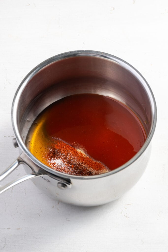 honey, hot sauce, and seasonings added to a small silver saucepan to make the spicy hot honey sauce.