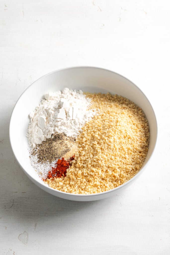 breadcrumbs, flour, and seasonings added to a bowl to make the chicken breading mixture before stirring together.