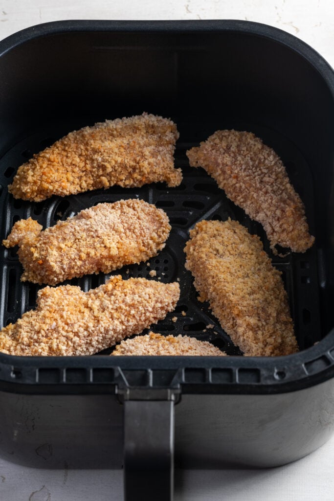 6 raw breaded chicken tenders in the base of an air fryer.