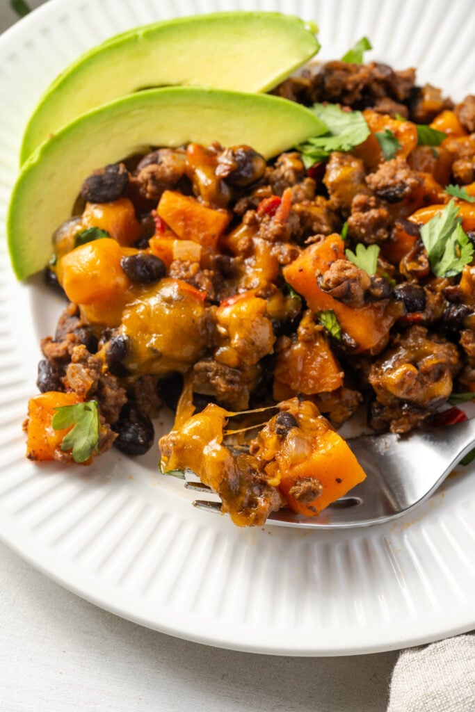 round white dinner plate with a serving of sweet potato and ground beef skillet topped with fresh cilantro and avocado slices.