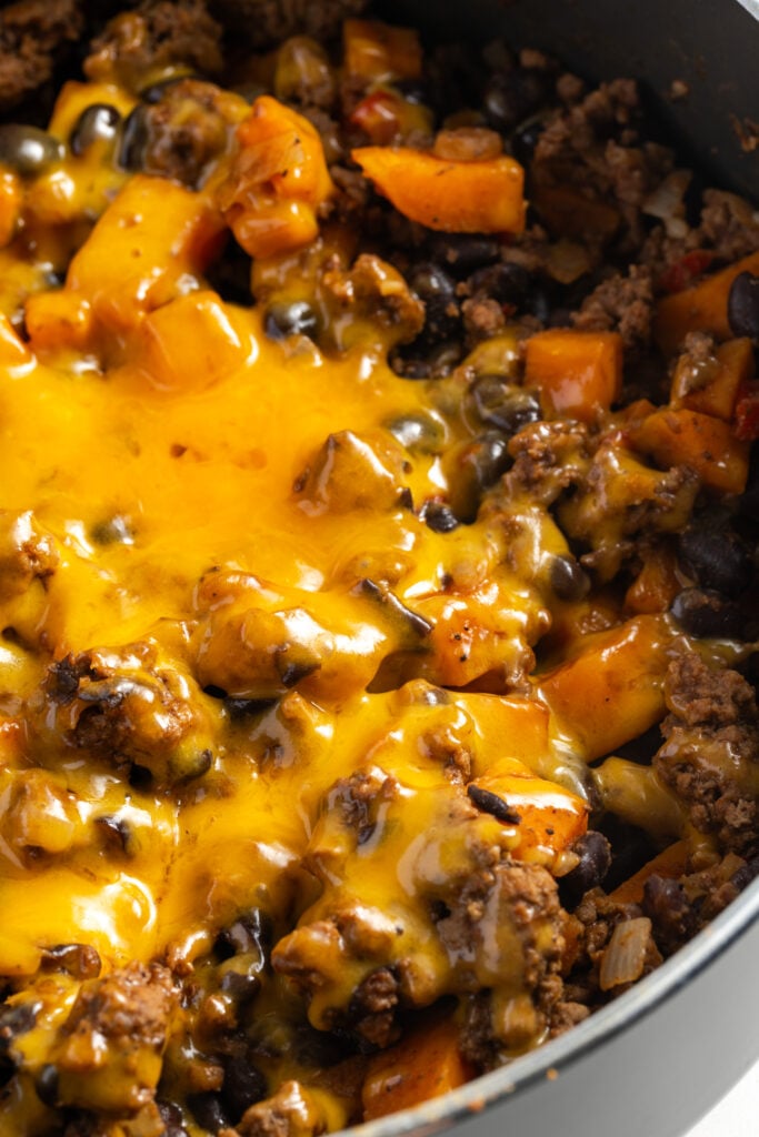 45 degree angle closeup of sweet potato ground beef skillet topped with melted cheddar cheese.