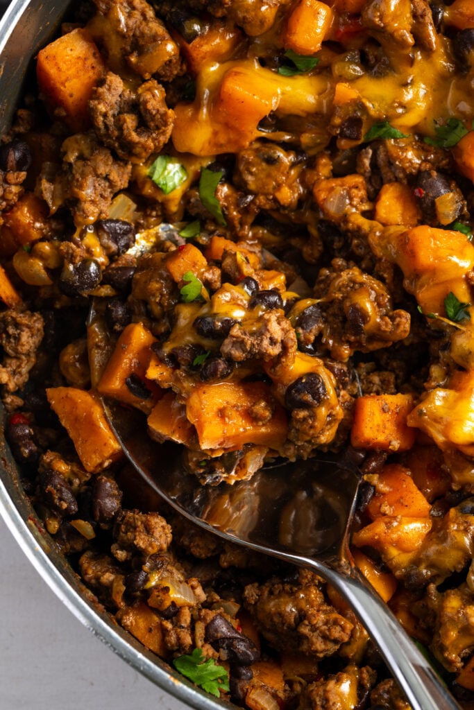 silver serving spoon in the cheesy ground beef sweet potato skillet scooping out a serving.