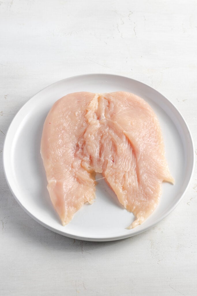 butterflied raw chicken breast on a white plate.