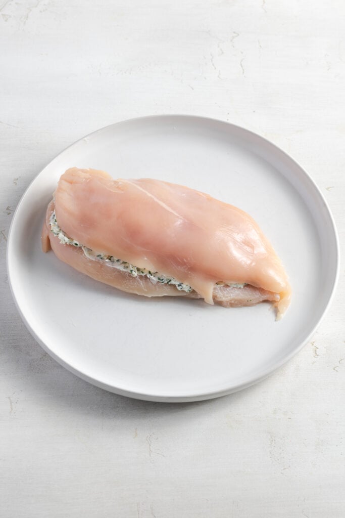 single chicken breast with cream cheese stuffing on a white plate.