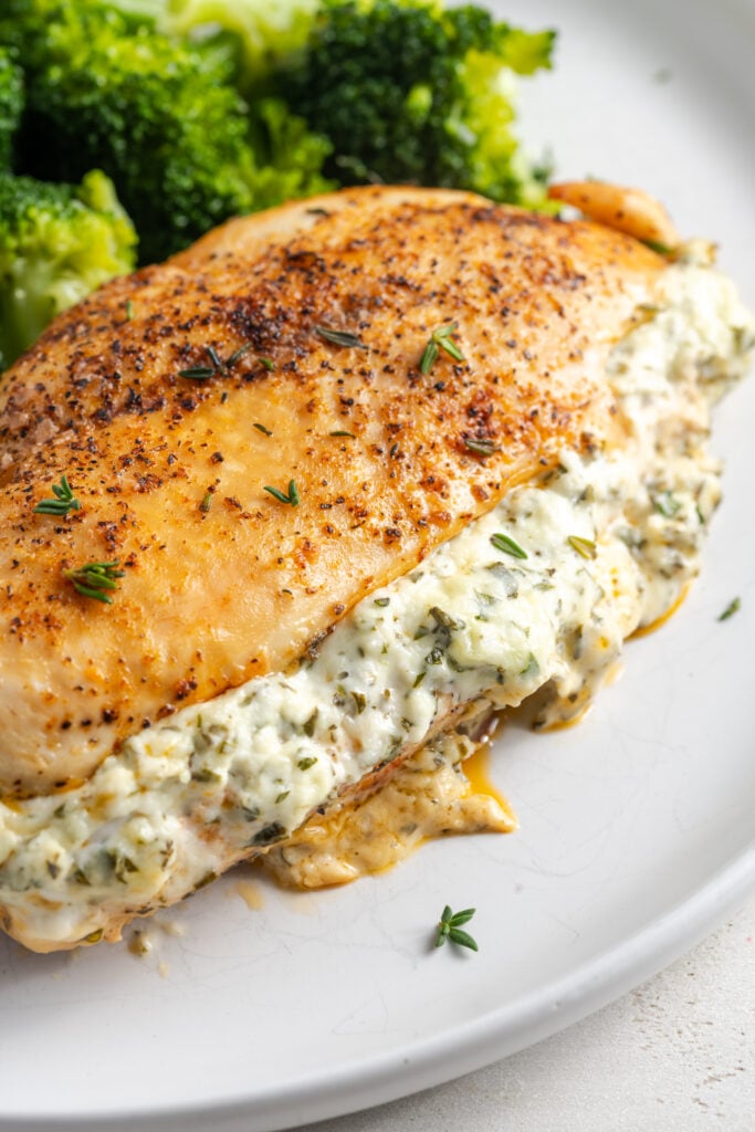 closeup shot of a whole cream cheese herb chicken breast on a white plate with broccoli.