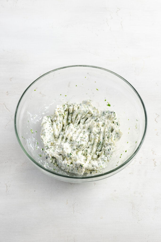 garlic herb cream cheese mixture in a small clear mixing bowl.