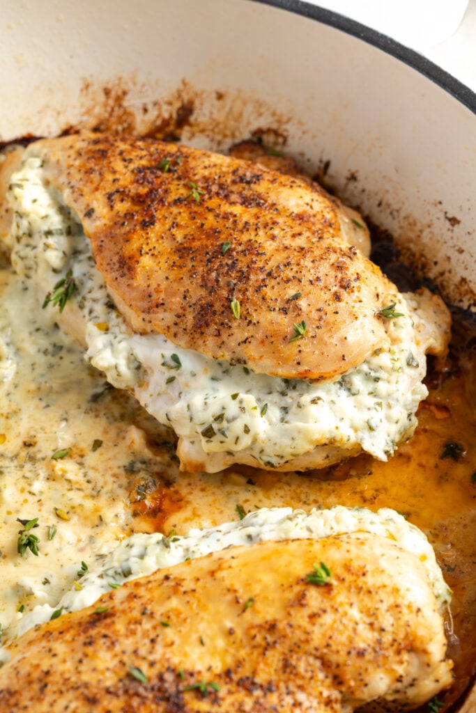 cream cheese stuffed chicken breast after cooking in a white cast iron pan with some of the juices surrounding it.