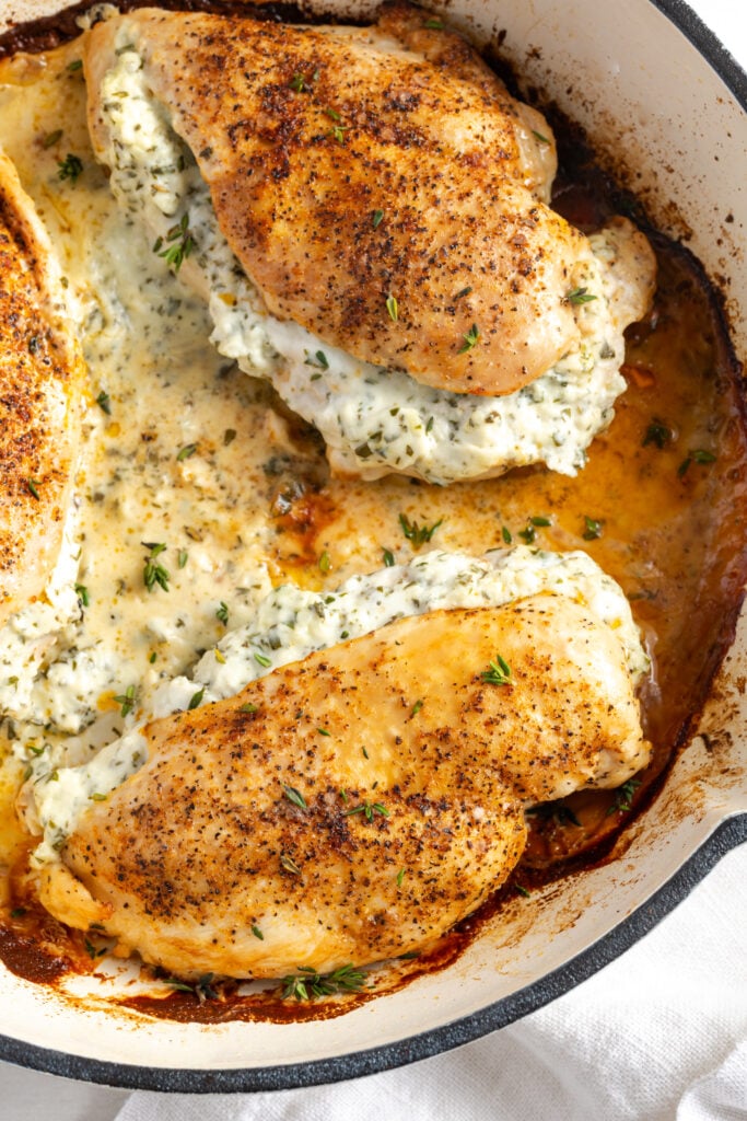 flat lay shot of cream cheese stuffed chicken breasts in a white cast iron pan after baking.