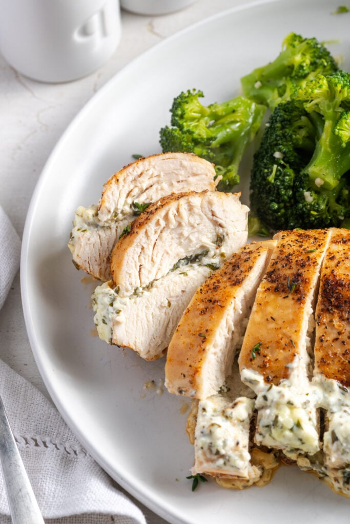 closeup shot of a plate of cream cheese stuffed chicken breast cut into slices revealing the juicy meat and pocket of filling.
