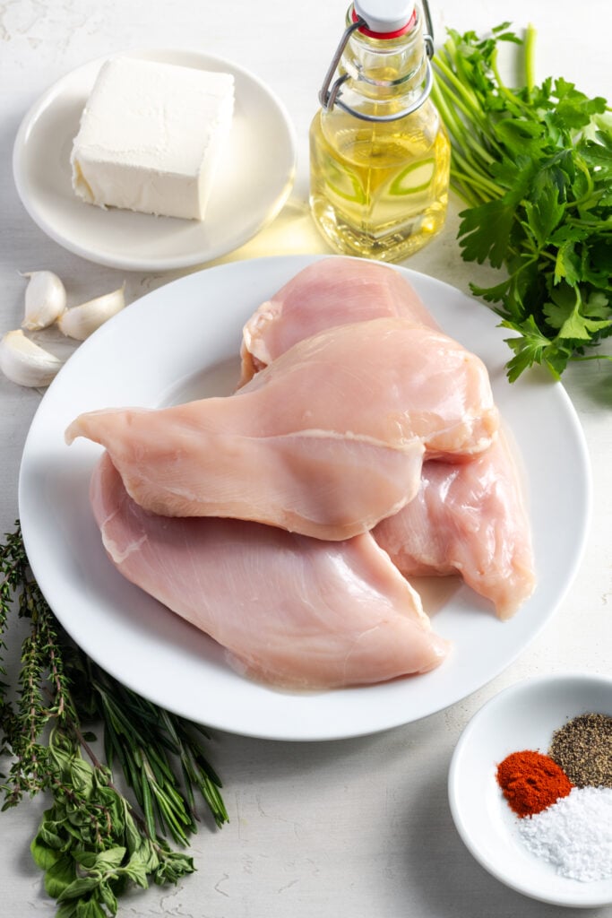 ingredients needed to make cream cheese stuffed chicken breasts measured out onto plates on a white table.
