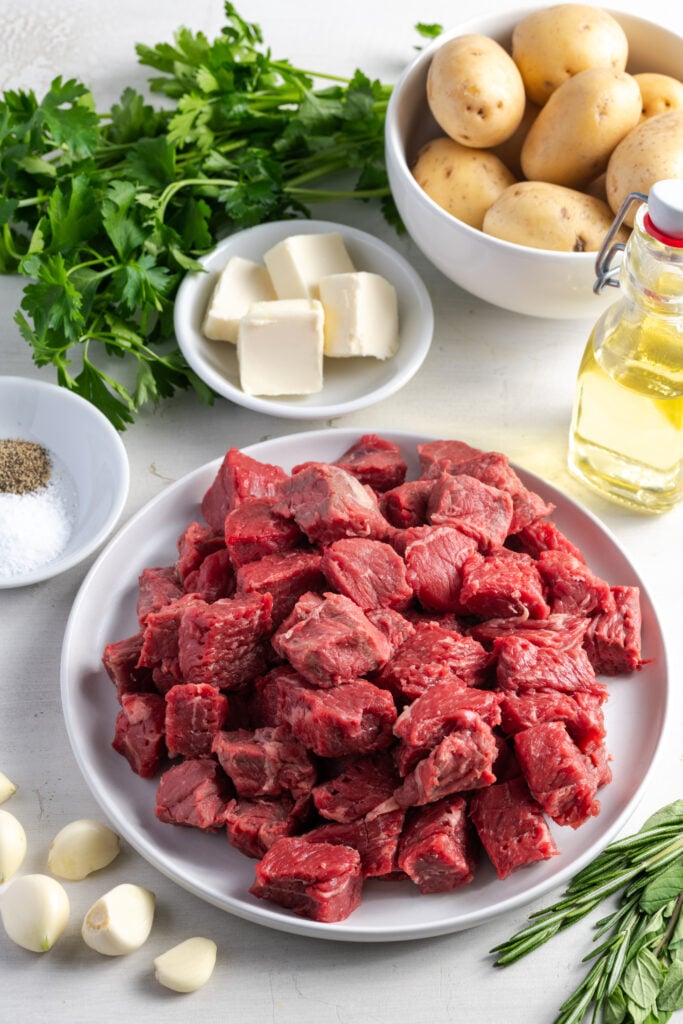 ingredients needed to make garlic butter steak bites and potatoes measured out into bowls and plates on a white table.