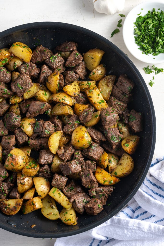 flat lay shot of a black skillet of garlic butter steak bites with potatoes and parsley.