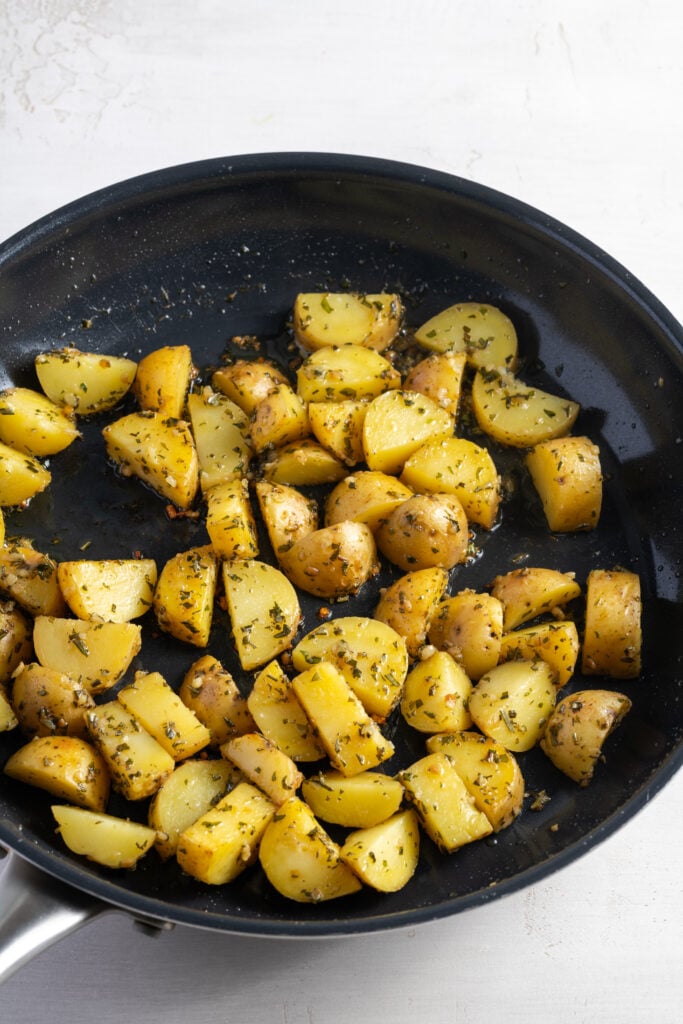 potatoes cooking in the pan with the garlic butter herb sauce spread all over them after tossing.