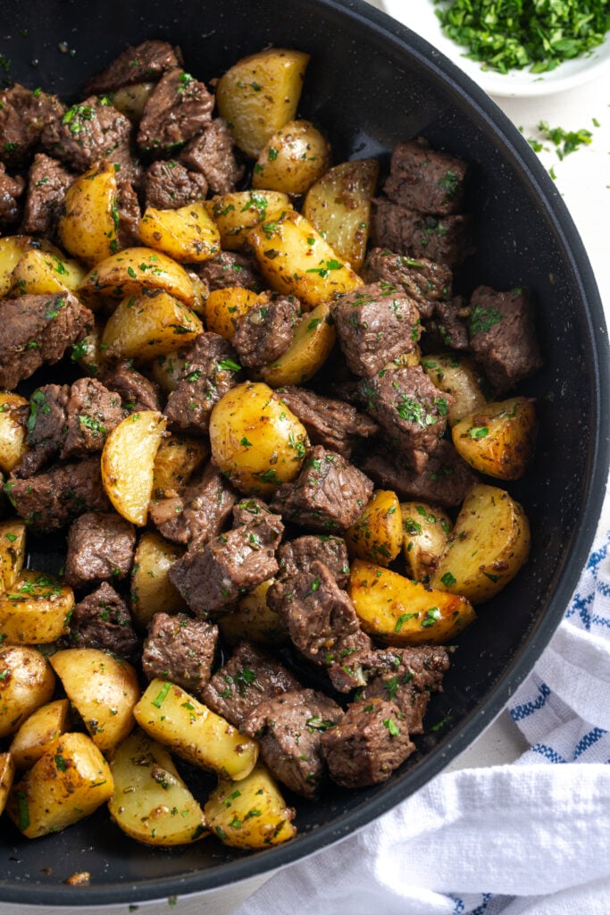 flat lay shot of garlic butter steak and potatoes skillet with the steak and potatoes cut into bite-sized chunks.