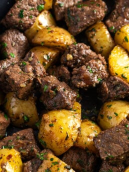 closeup shot of steak bites and potatoes in garlic butter garnished with fresh parsley.