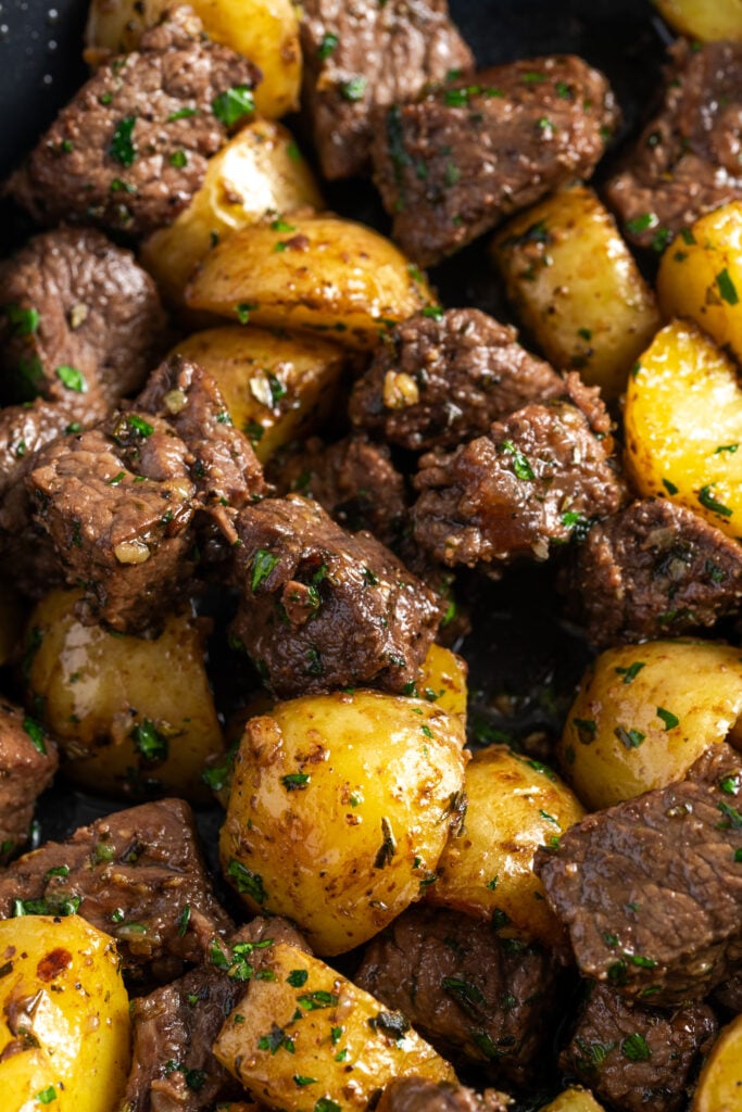 closeup shot of steak bites and potatoes in garlic butter garnished with fresh parsley.