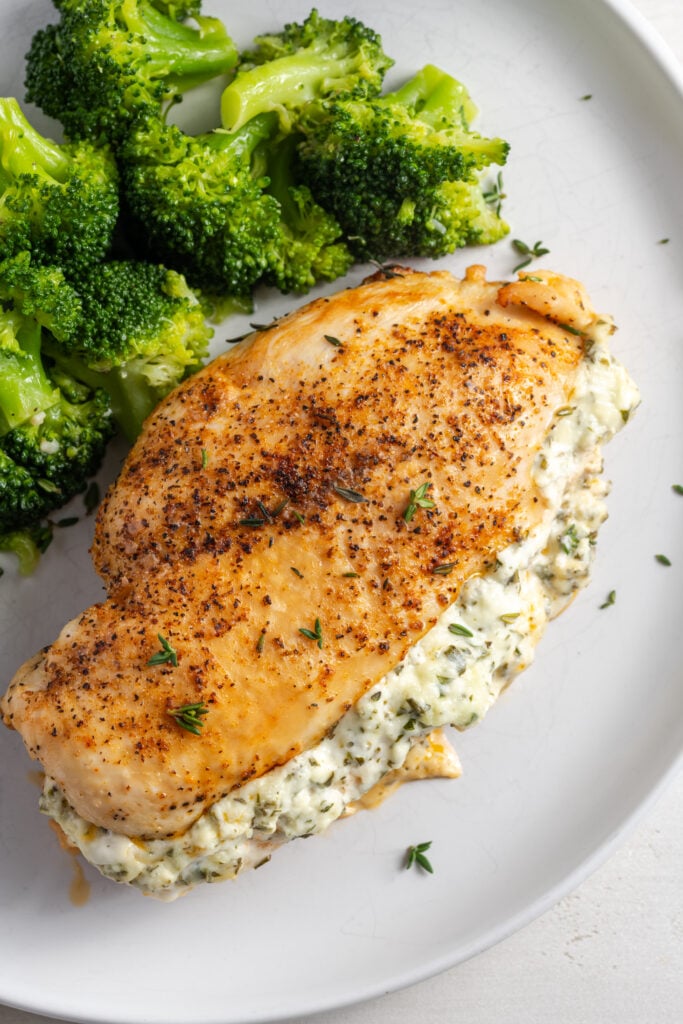 overhead shot of stuffed cream cheese chicken breast with steamed broccoli on a white dinner plate.
