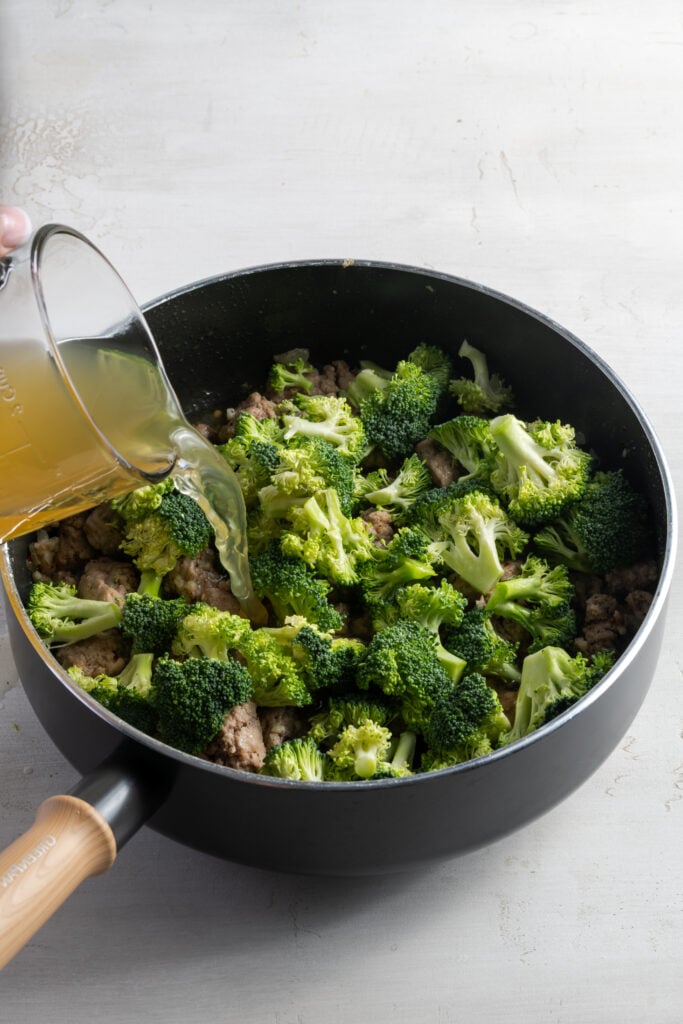 chicken broth being added to the pan with the broccoli and ground turkey to make one-pot pasta.