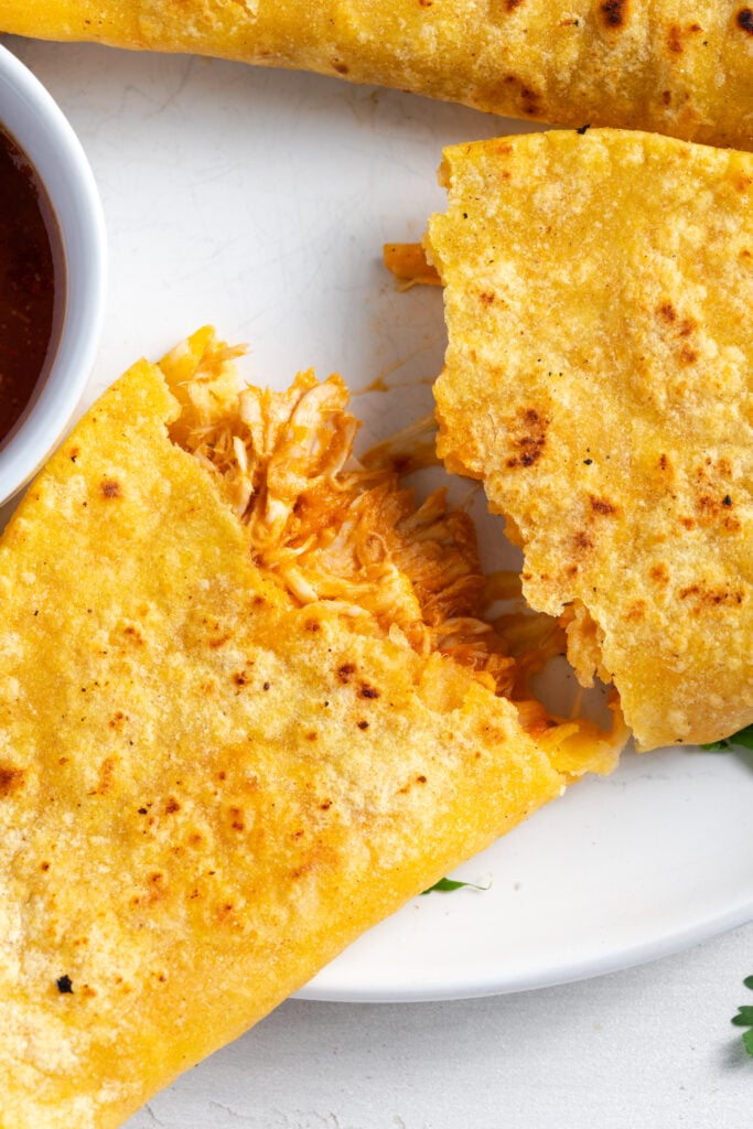 closeup shot of a crispy chicken and cheese taco that has been pulled into two halves with the chicken and cheese filling pulled between the sides.