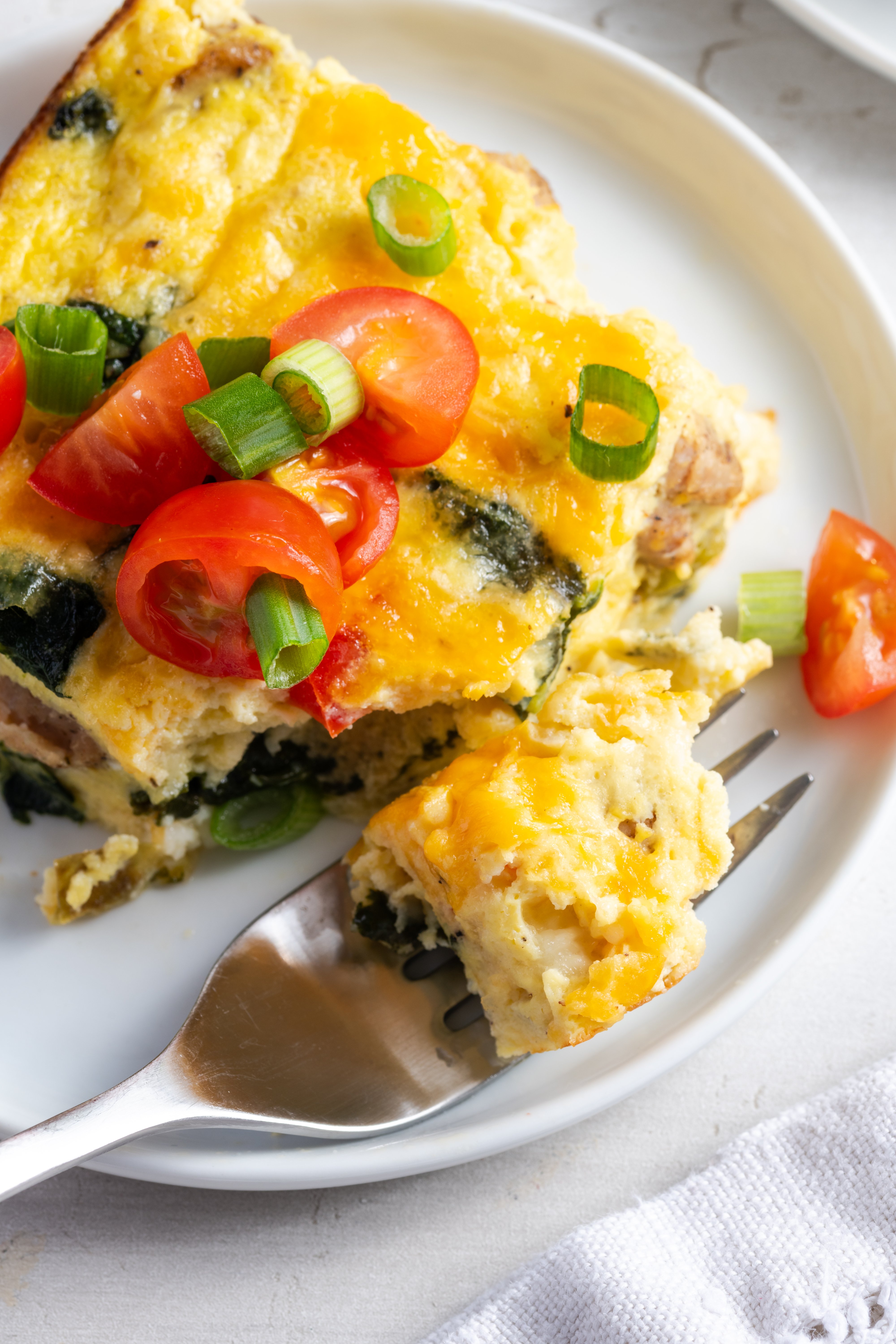 slice of easy cottage cheese egg bake on a small round white plate with a silver fork taking a bite out of it.