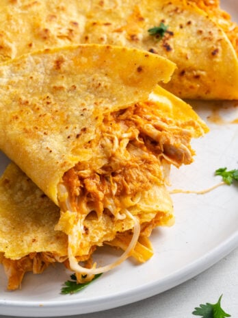 closeup shot of a halved crispy chicken taco showing the saucy chicken and melty cheese inside.
