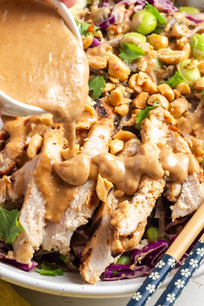 action shot of Thai peanut salad dressing being drizzled over the chicken on top of the noodle salad.