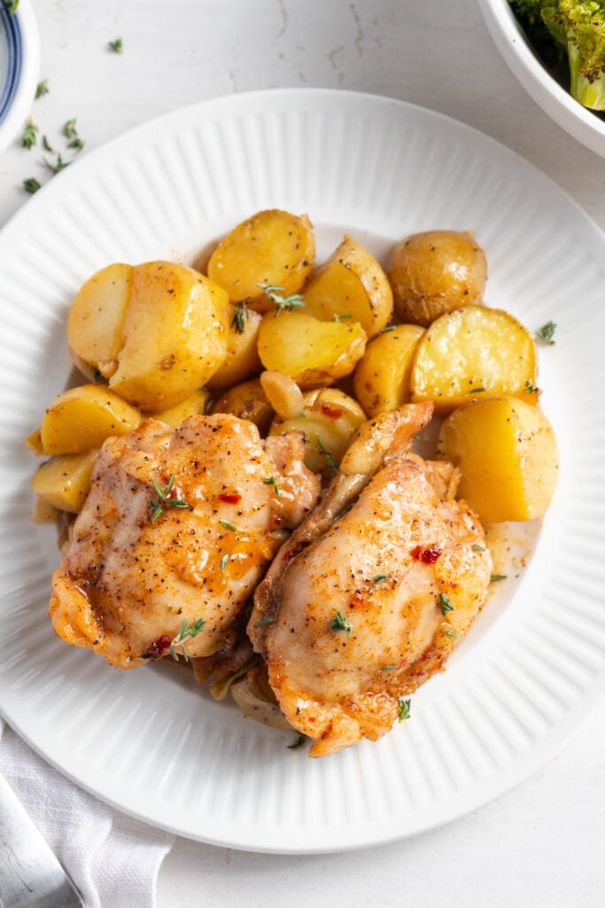 two chicken thighs and roasted potatoes on a plate for serving.