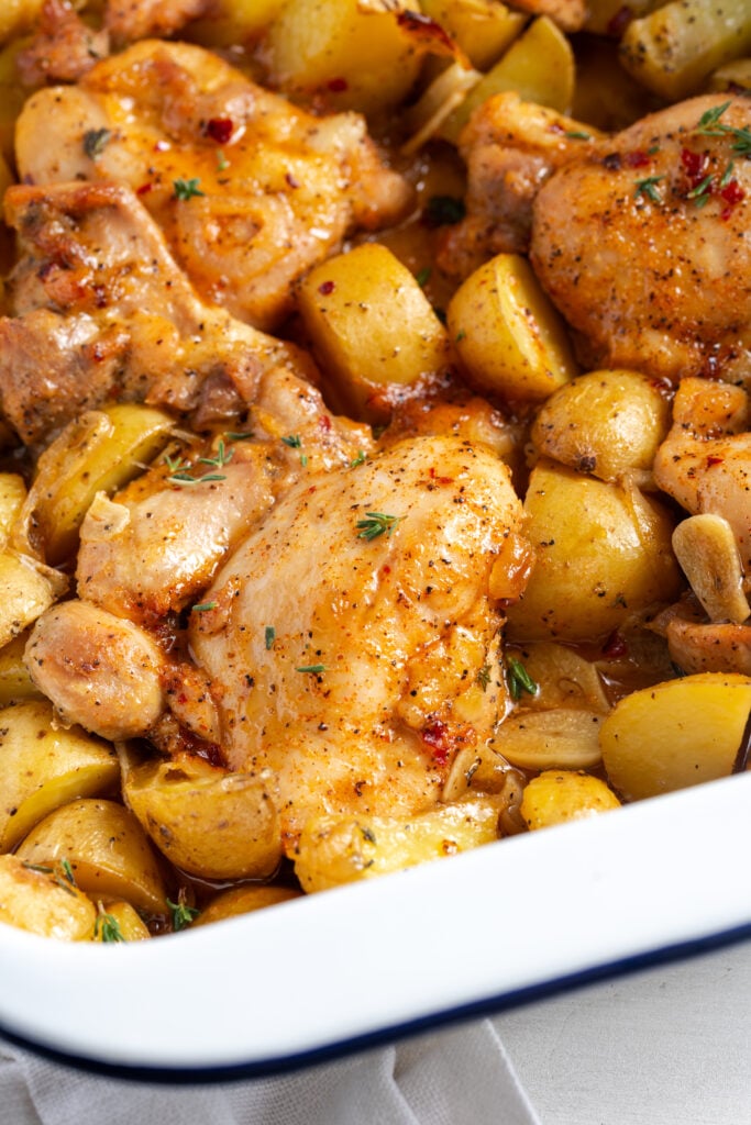 closeup shot of the bottom left corner of a white 9x13 pan filled with potatoes and chicken thighs in a saucy marinade after baking.