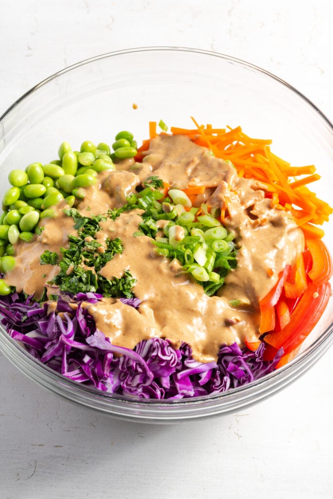 peanut noodle salad dressing drizzled on top of the veggies in the mixing bowl.