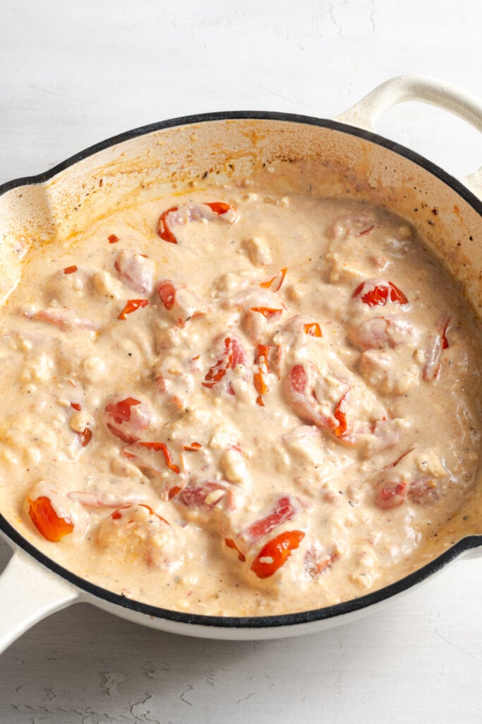 feta tomato sauce in the white skillet after removing the chicken and stirring the sauce together.