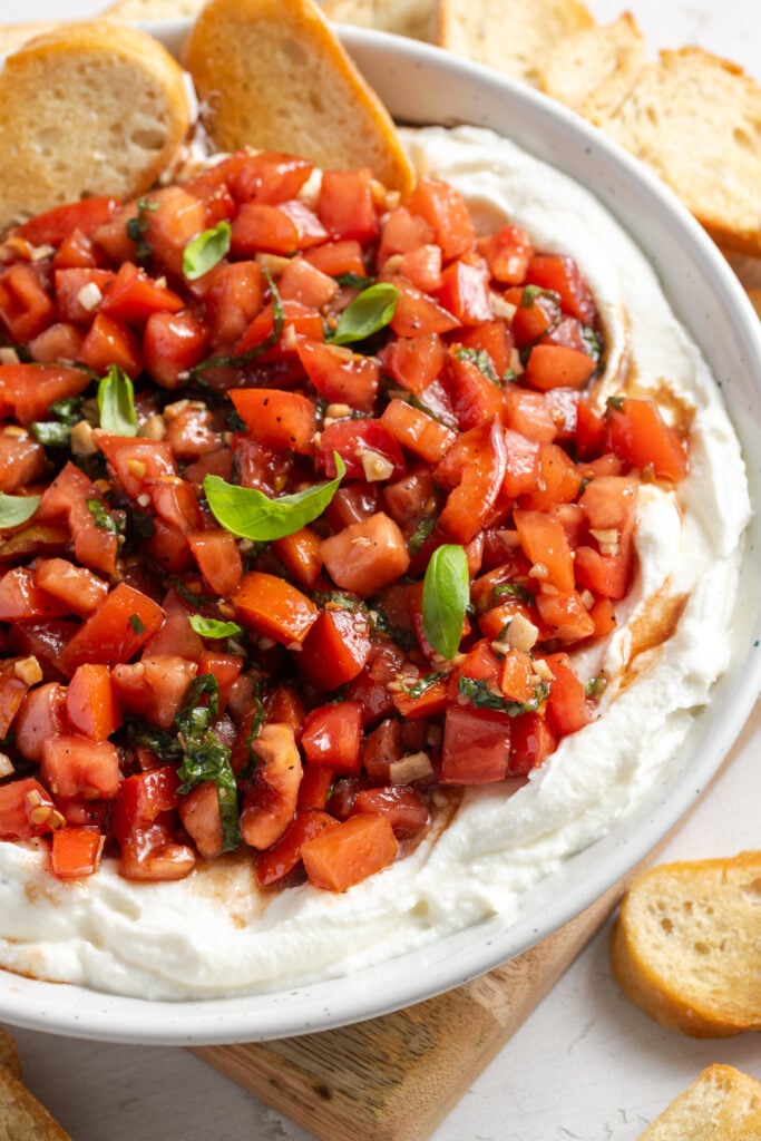 45 degree angle shot of bruschetta dip with whipped ricotta and crispy homemade crostini for dipping.