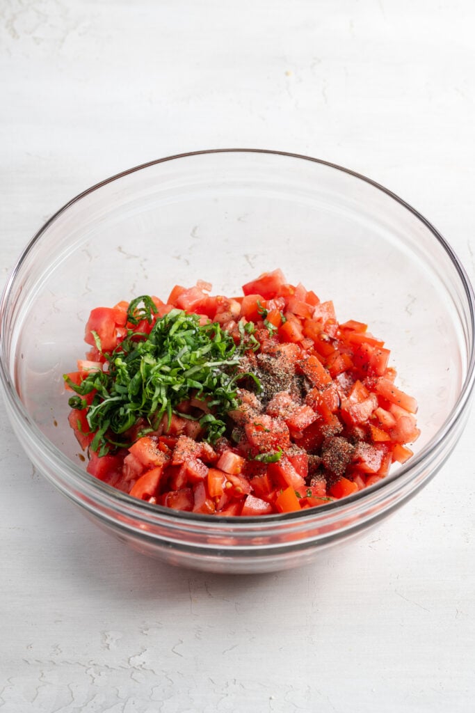 bruschetta topping ingredients added to a clear mixing bowl.