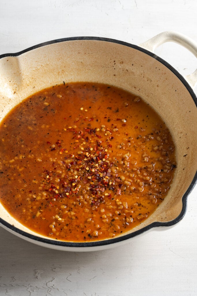 chicken broth, garlic, and seasonings in a skillet after deglazing.