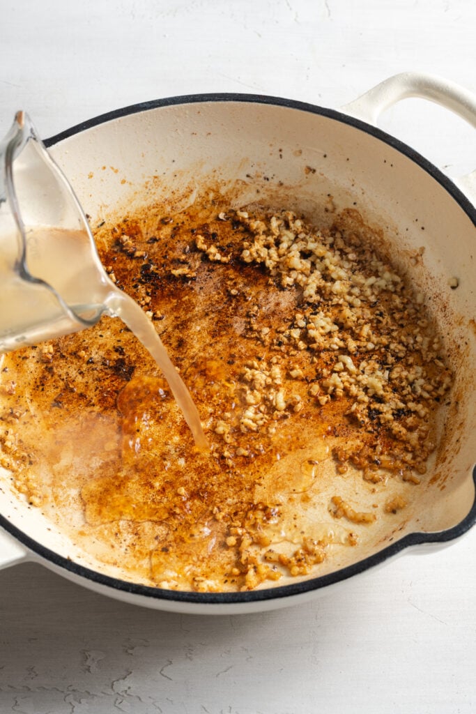 action shot of chicken broth being poured into the skillet to deglaze the pan.