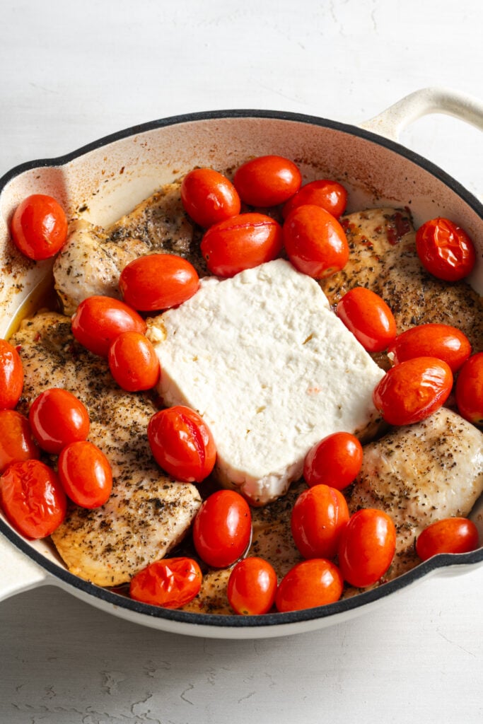 chicken feta tomato skillet after baking; the feta is still in a block and tomatoes are whole but wrinkly from the heat.