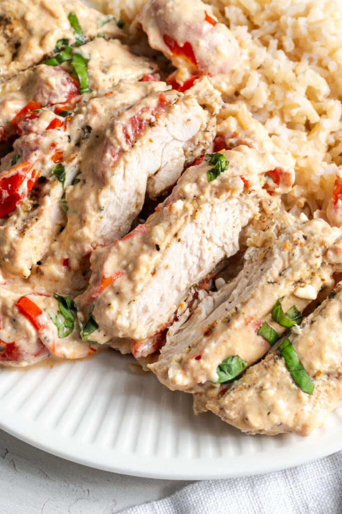 closeup shot of creamy feta tomato baked chicken; the breast has been sliced to show the juicy interior.