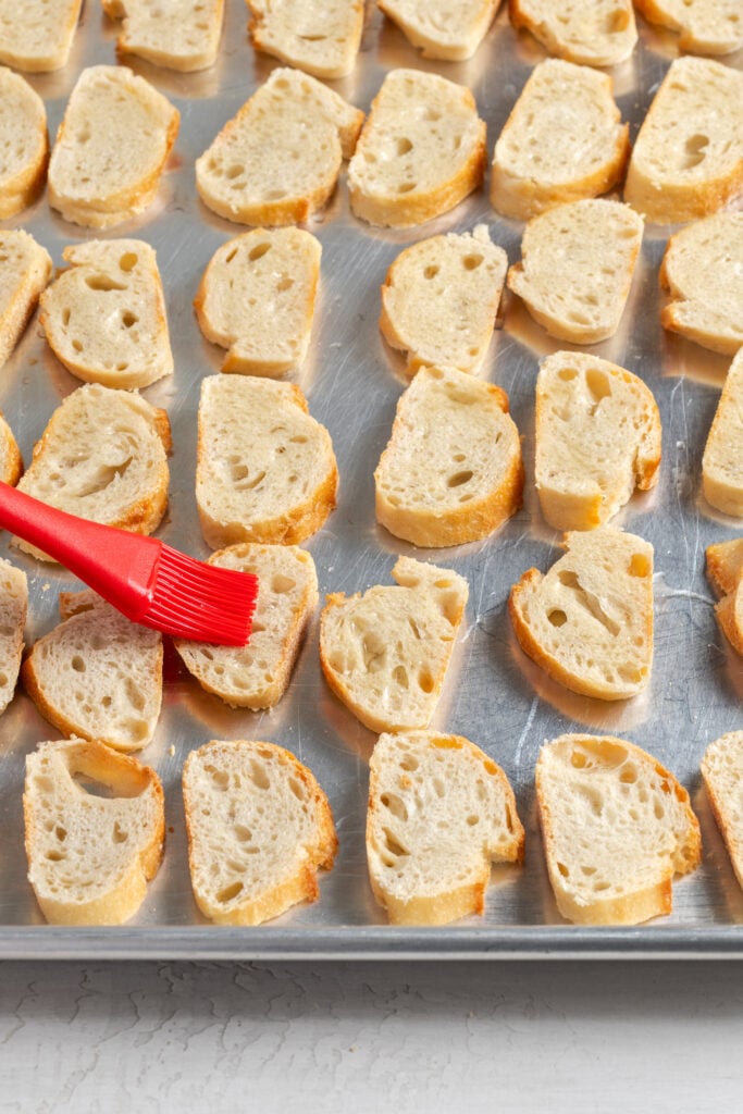 action shot of a pastry brush brushing the bread slices with oil.