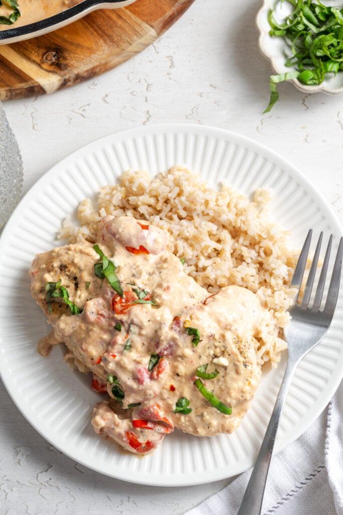 dinner plate with feta and tomato chicken topped with basil chiffonade on a white table with a small pinch bowl of extra basil and a wooden cutting board in the top of the frame.