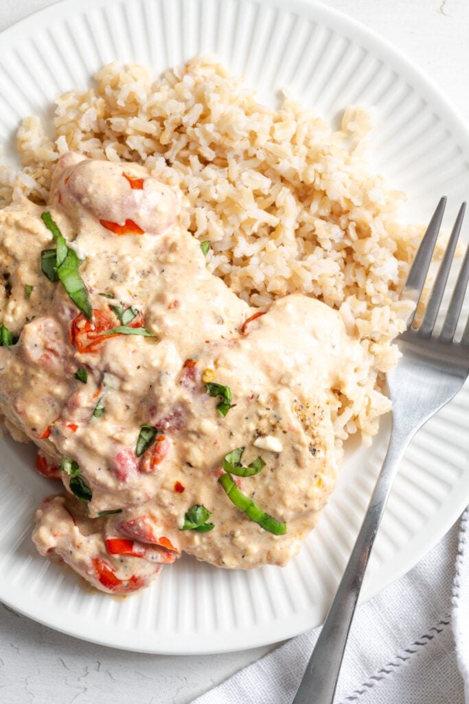 overhead closeup shot of feta and tomatoes baked chicken in a creamy sauce on a bed of brown rice.