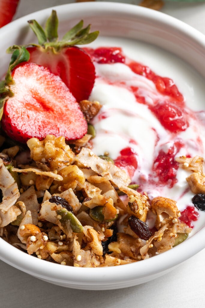 closeup shot of a small bowl of yogurt topped with grain-free oat free granola and strawberry jam.