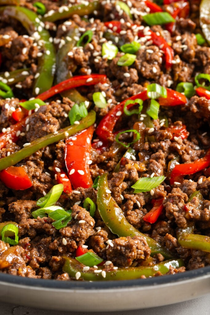 closeup shot of ground beef and bell peppers stir fry mixture in the skillet topped with scallion greens and sesame seeds.