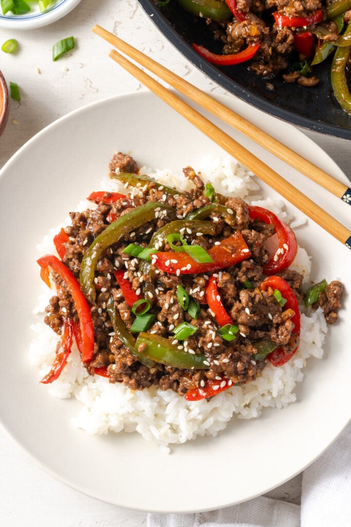 flat lay shot of a white pasta bowl filled with rice topped with ground beef and pepper stir fry.