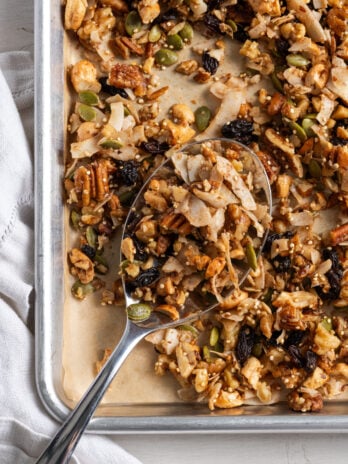 silver spoon on the bottom left corner of a parchment lined baking sheet scooping up some healthy grain free granola.