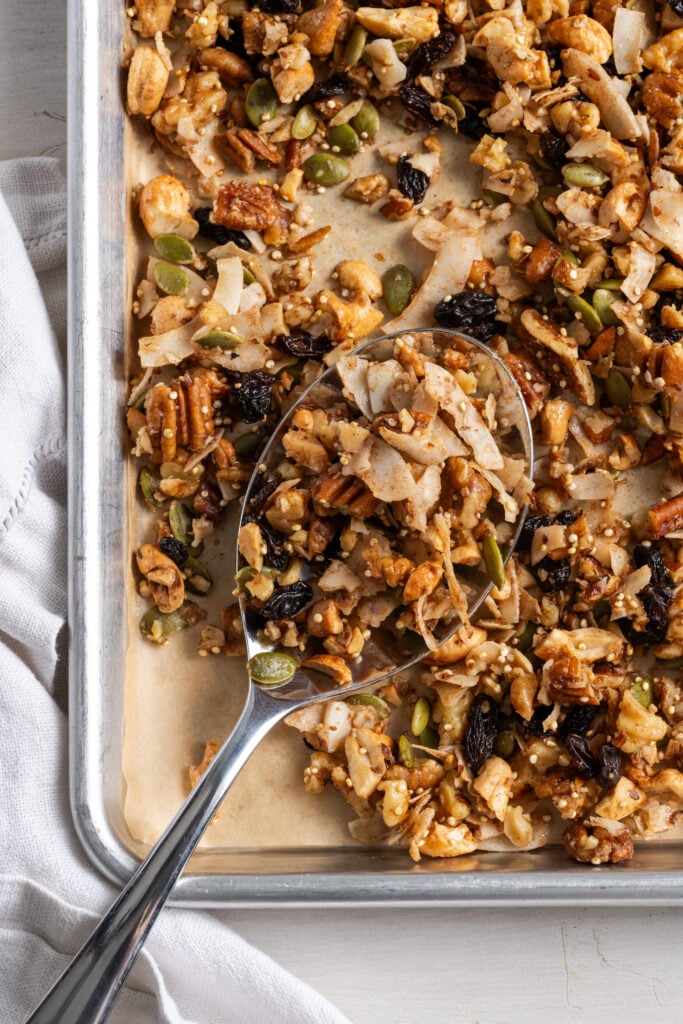 silver spoon on the bottom left corner of a parchment lined baking sheet scooping up some healthy grain free granola.