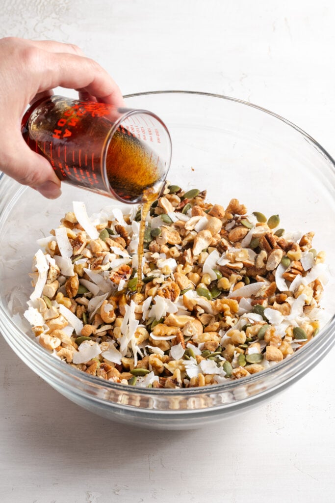 action shot of hand pouring the liquid ingredients over the dry grain free granola mixture.