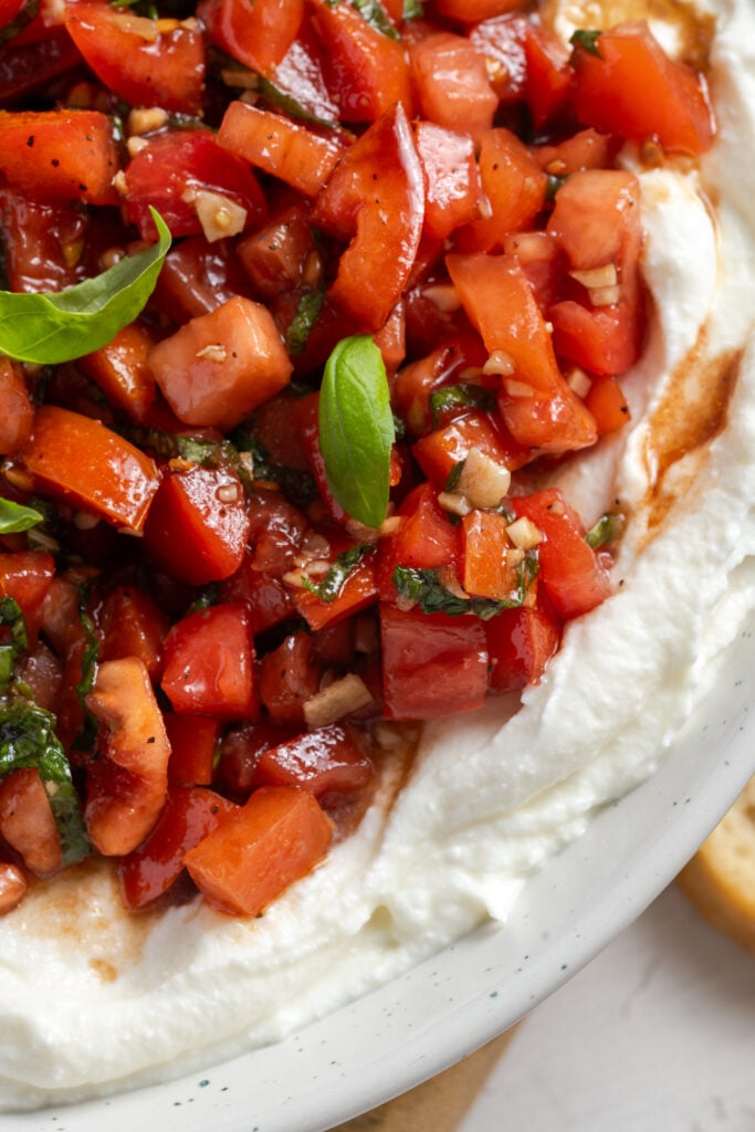 closeup overhead shot of ricotta bruschetta dip showing the juicy balsamic tomato mixture and fluffy texture of the ricotta.