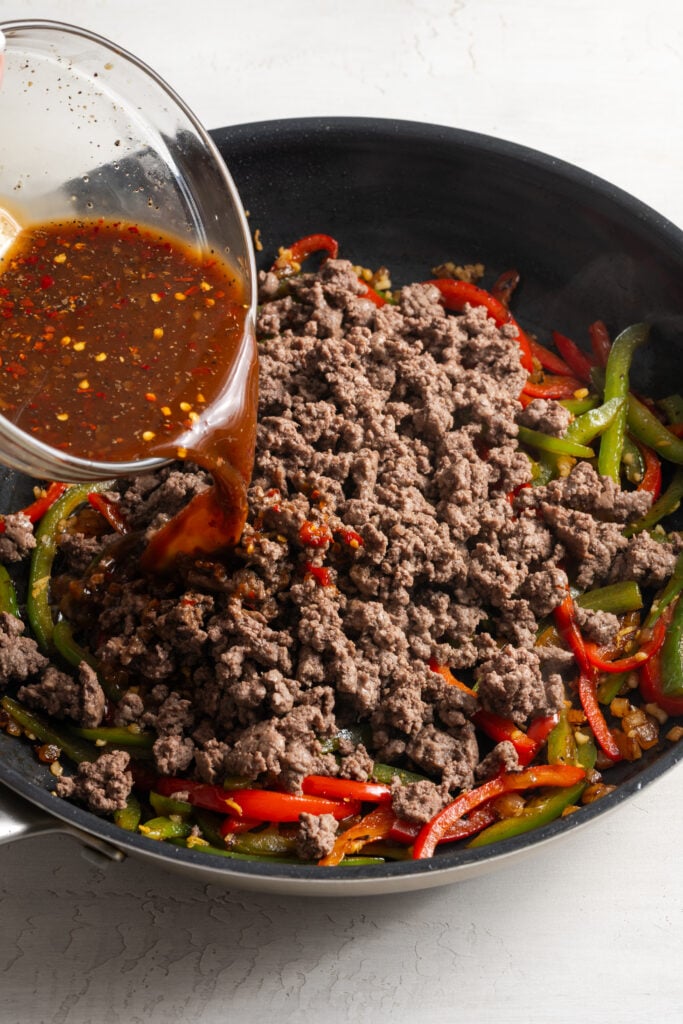 honey soy garlic sauce being poured over the ground beef and peppers in the skillet.