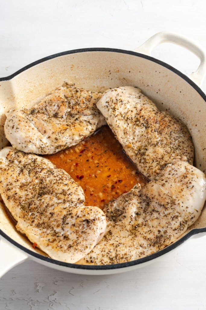 seared chicken in a skillet with a bit of broth.
